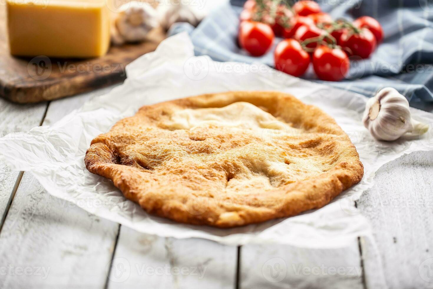 tradizionale ungherese piatto langos servito su un' cottura al forno carta nel il sfondo con aglio pomodori e formaggio su un' di legno piatto foto