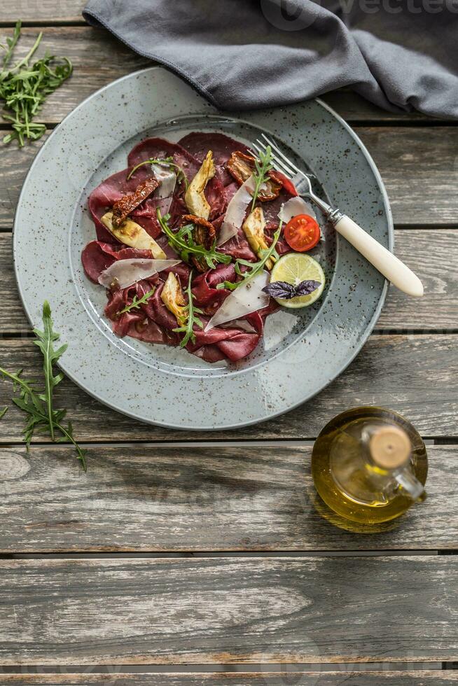 Manzo carpaccio su piatto con secco pomodori carciofi rucola e parmigiano formaggio foto