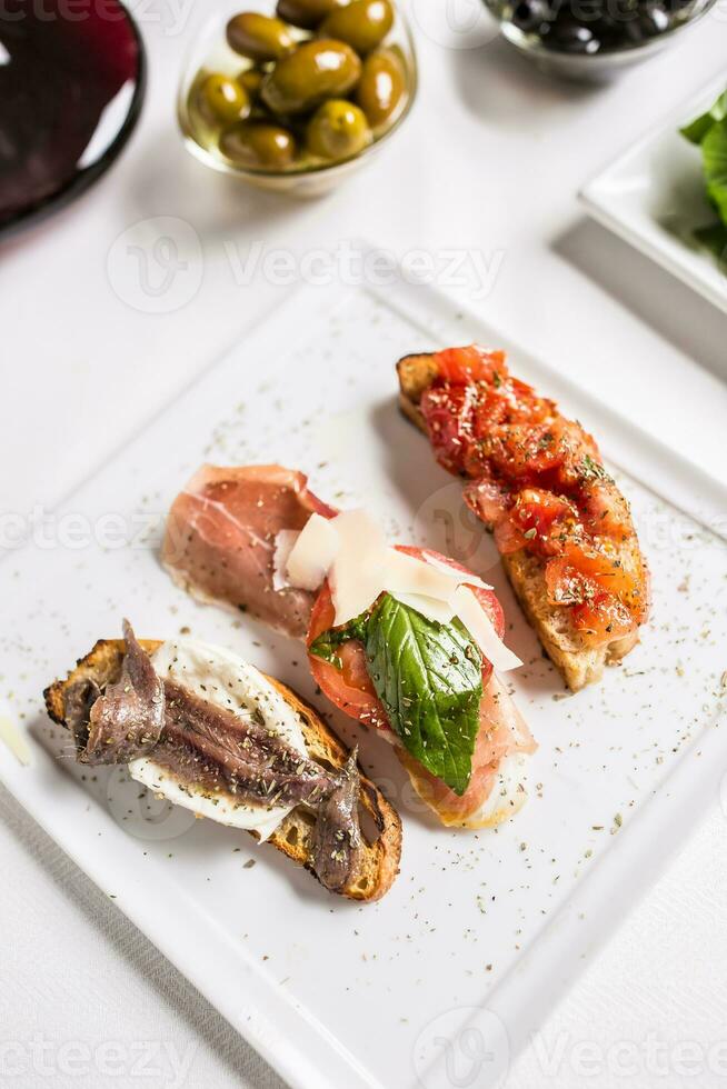 gustoso italiano aperitivo bruschette con pomodori acciughe prosciutto e mozzarella foto