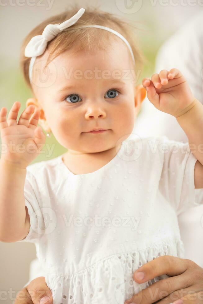adorabile piccolo bambino piccolo ragazza con blu occhi e bionda capellicon sua braccia sollevato per sua testa foto