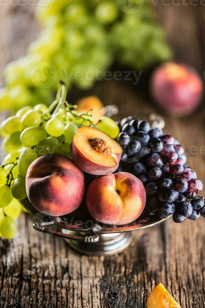 maturo uva e Pesche nel rustico ciotola e di legno tavolo foto