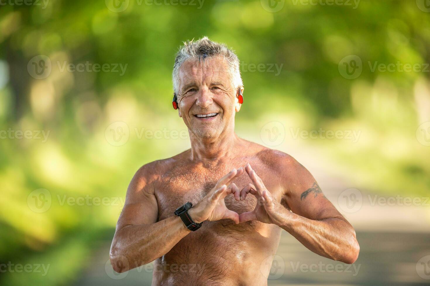 vecchio ma in forma uomo con grigio capelli Spettacoli un' cuore gesto con il suo dita come un' cartello di il suo salutare cardiovascolare sistema foto