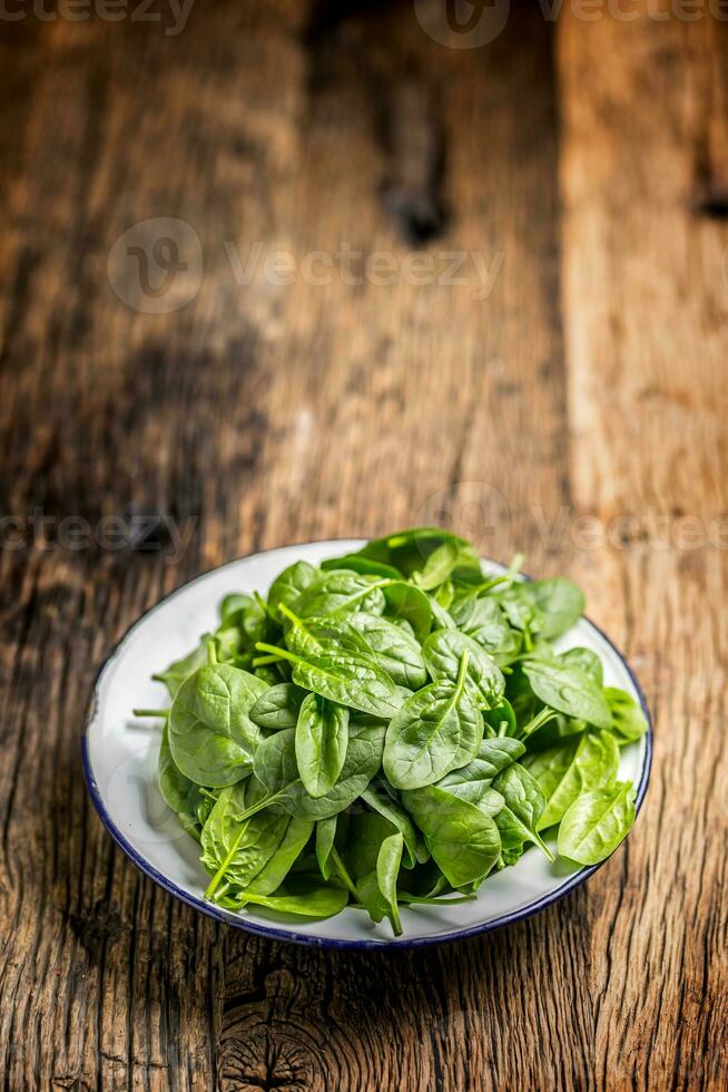 spinaci. fresco bambino spinaci le foglie nel piatto su woden tavolo foto