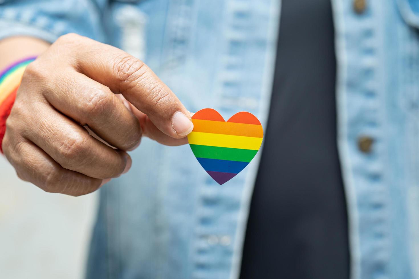 la signora asiatica che indossa una giacca di jeans blu o una camicia di jeans e tiene in mano il cuore della bandiera color arcobaleno, simbolo del mese dell'orgoglio lgbt celebra l'annuale a giugno sociale di gay, lesbiche, bisessuali, transgender, diritti umani. foto