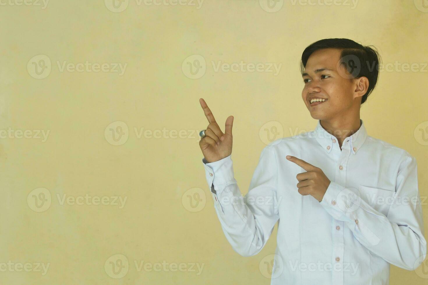 giovane asiatico uomo puntamento sinistra con dito isolato su giallo sfondo foto