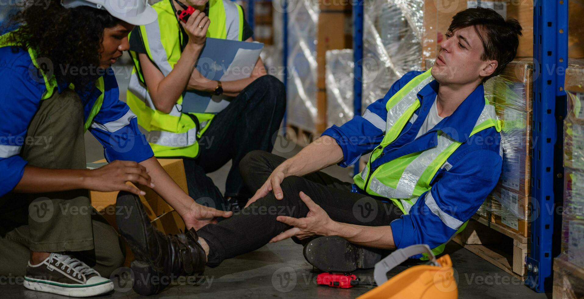 un' magazzino lavoratore abbattere dopo inciampare su alcuni detriti. lui è stringendo il suo caviglia nel dolore come Due supervisori assistere lui. foto