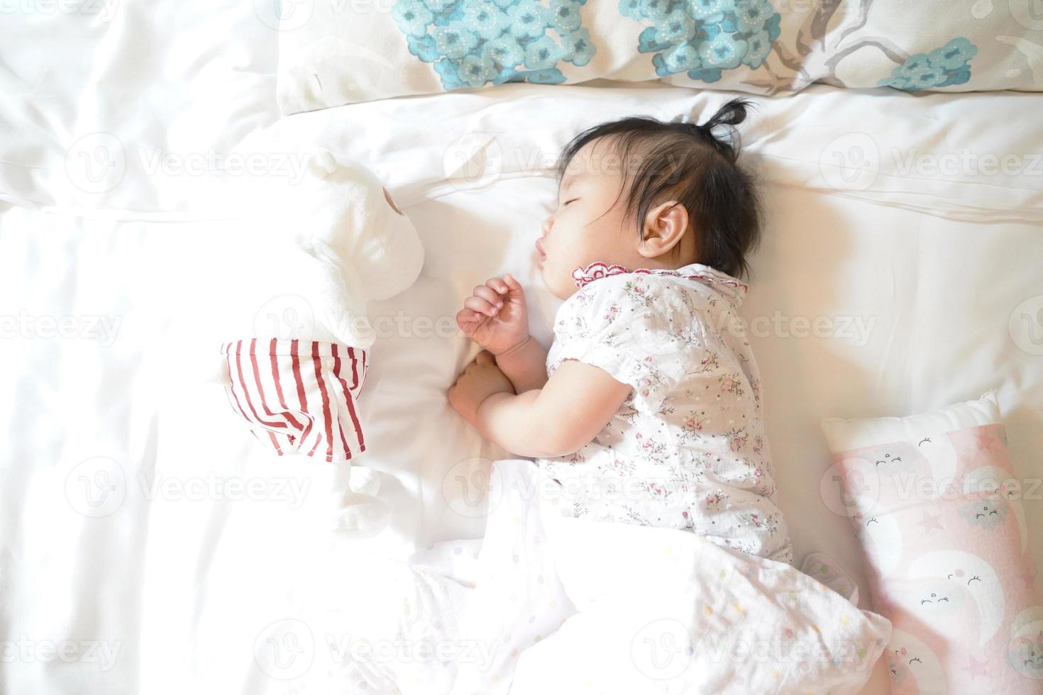 carino assonnato 1 anni bambina asiatica che dorme su un morbido letto con una bambola, concetto neonato. foto