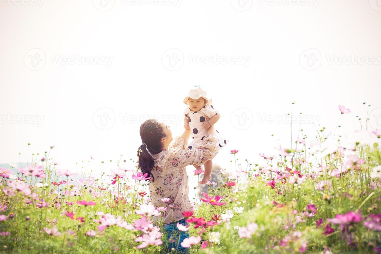 la giovane madre asiatica con la sua bella figlia riccia stanno camminando nel giardino primaverile con fiori di rose rosa in fiore, ora del tramonto. vacanza in famiglia in giornata estiva. foto