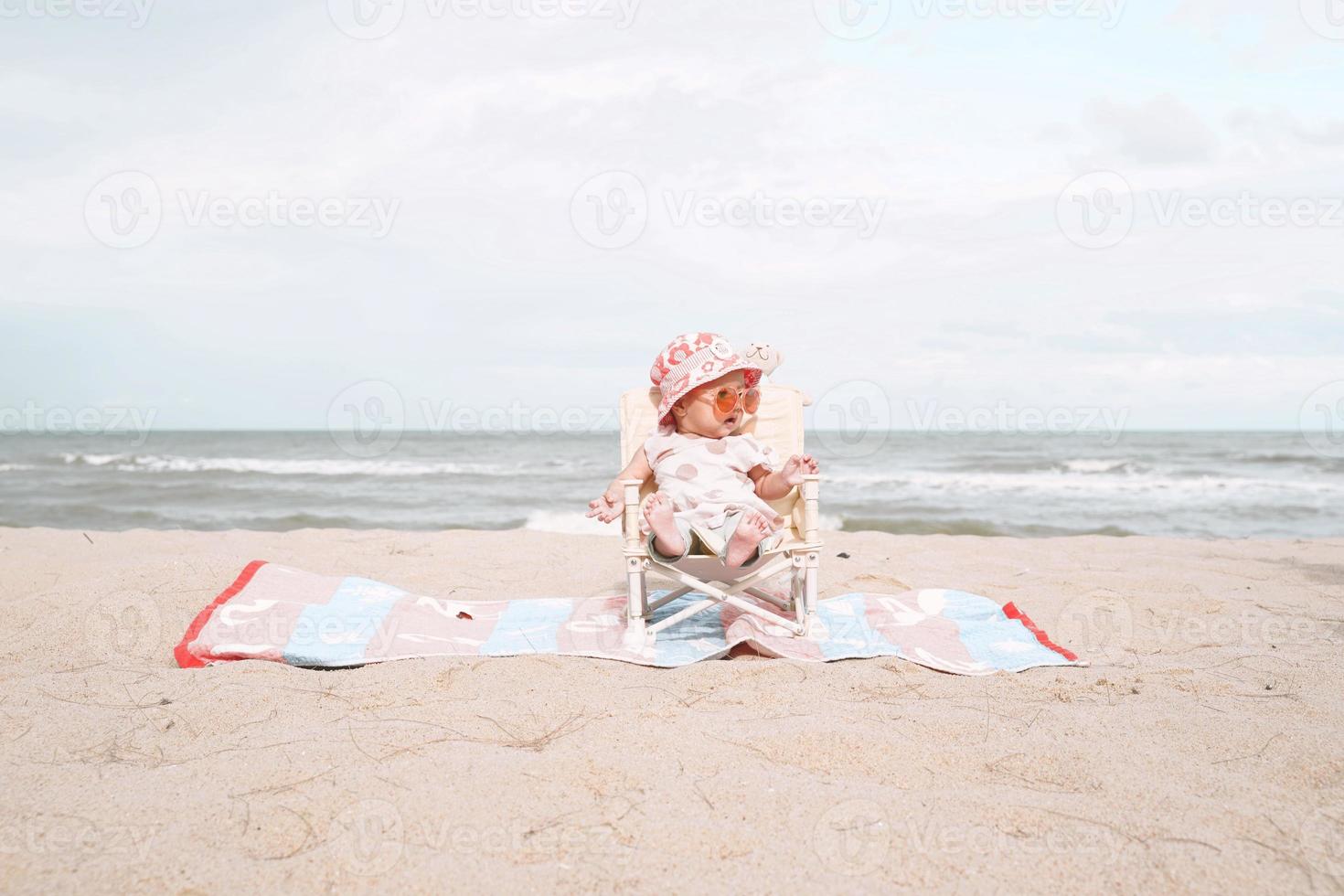 bambina asiatica seduta sulla sedia a sdraio e indossando occhiali da sole. foto