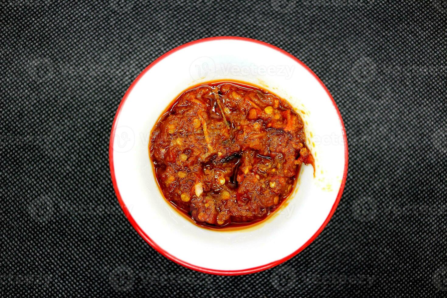 Giava speziato chili salsa nel un' bianca piatto su un' nero sfondo foto
