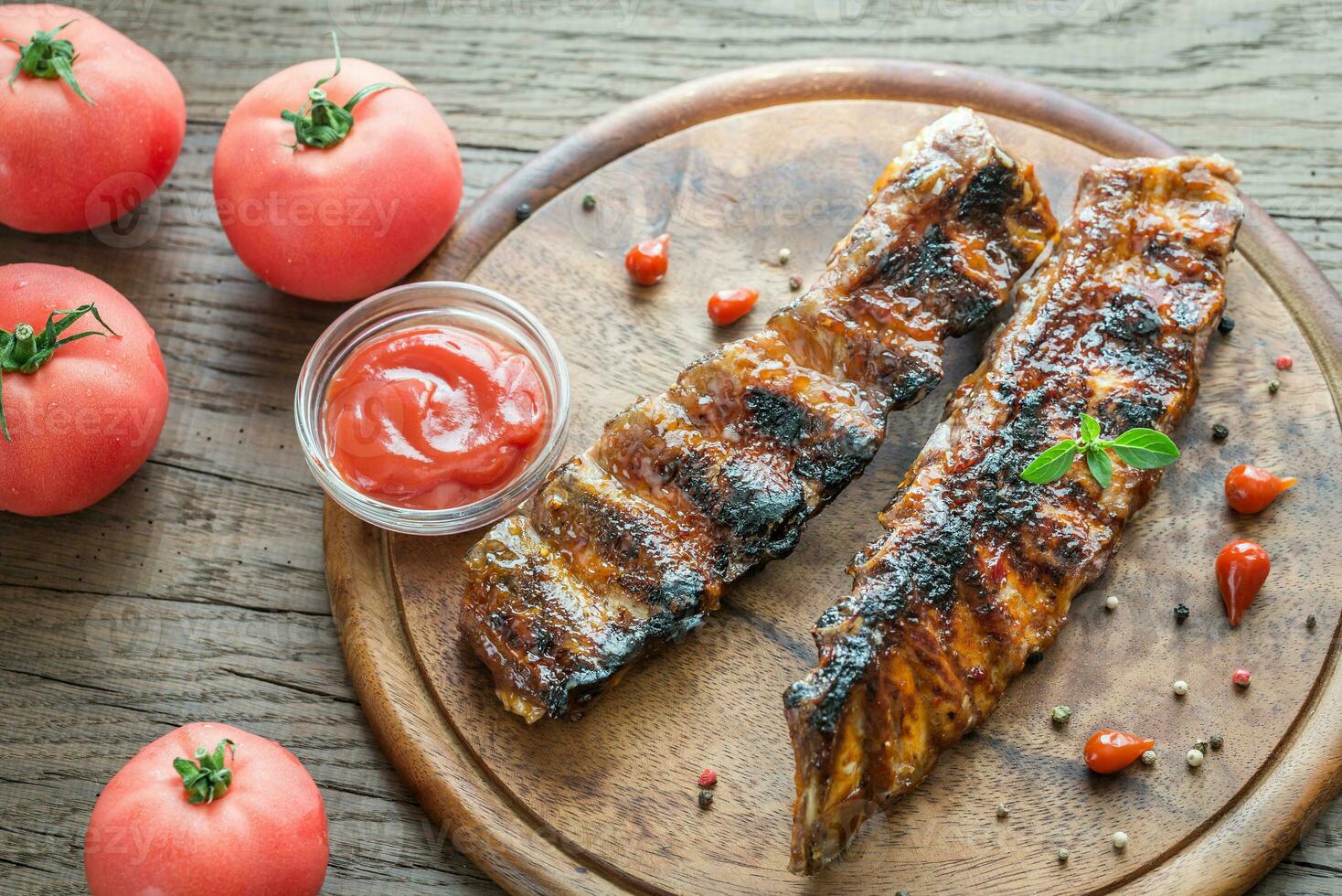 costolette di maiale alla griglia con pomodori sulla tavola di legno foto