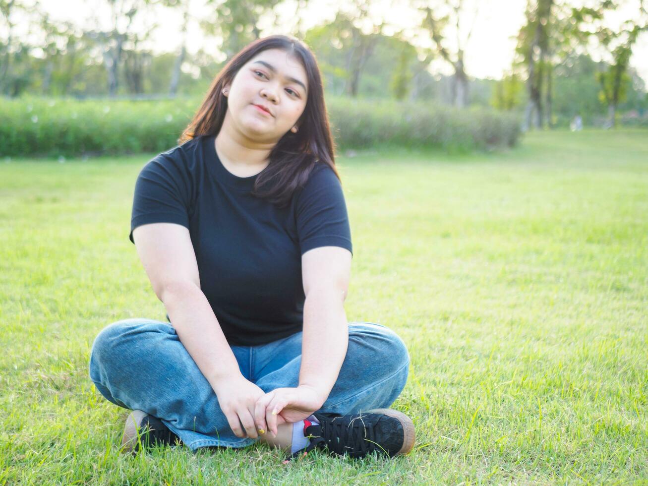 ritratto giovane donna ragazza asiatico paffuto carino bellissimo lungo nero capelli uno persona indossare nero camicia seduta con braccia sollevato liberamente nel giardino parco all'aperto sera luce del sole fresco contento rilassare sumer giorno foto