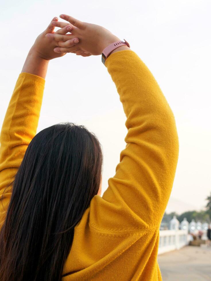 ritratto 30 anno vecchio Grasso asiatico donna con lungo nero capelli indossare lungo maniche giallo maglietta. in piedi con mani e braccia sollevato allungare pigramente corpo rilassare felicemente e liberamente su giorno via a partire dal sua opera foto