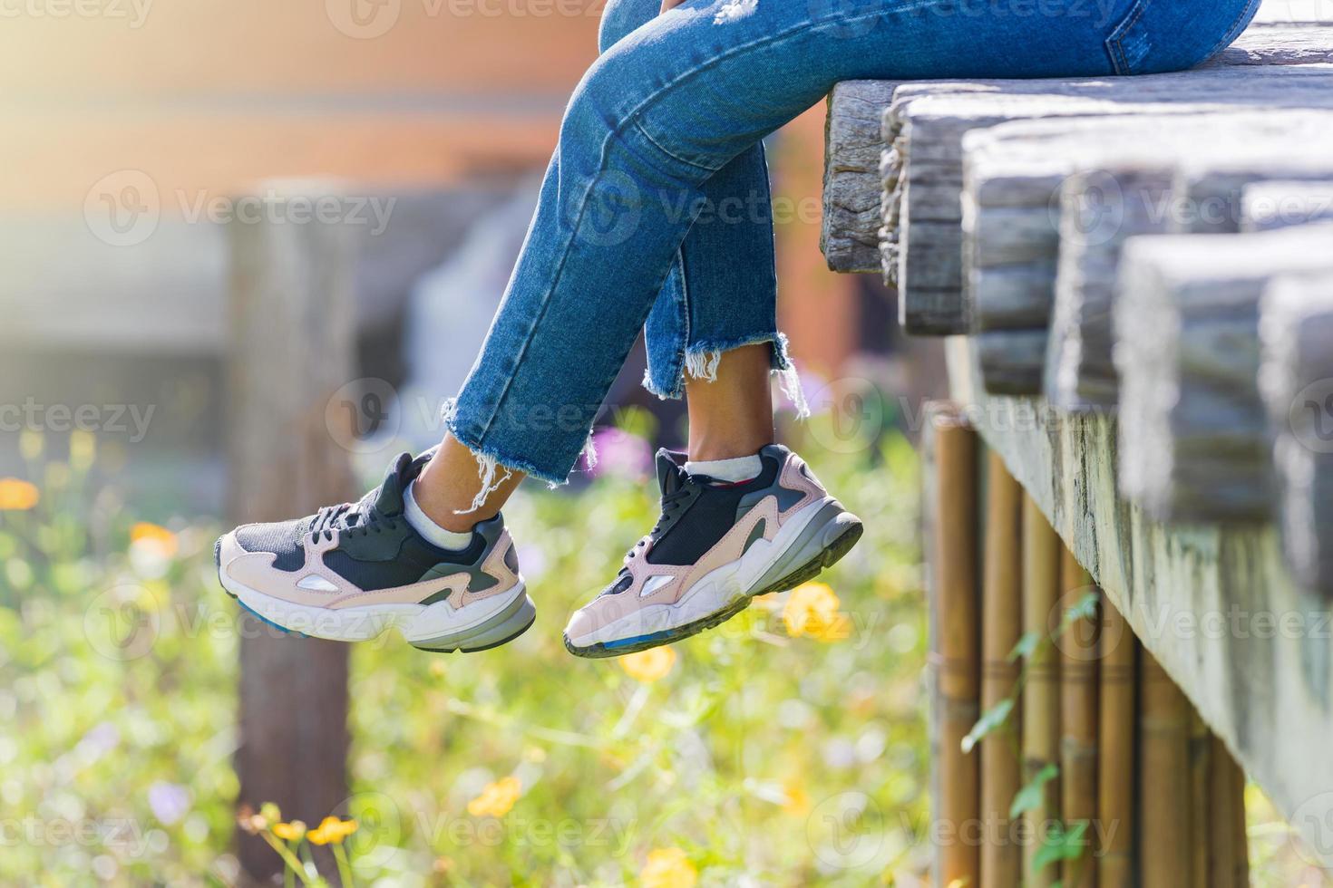 donna seduta sul ponte di legno e gambe appese nel giardino fiorito foto