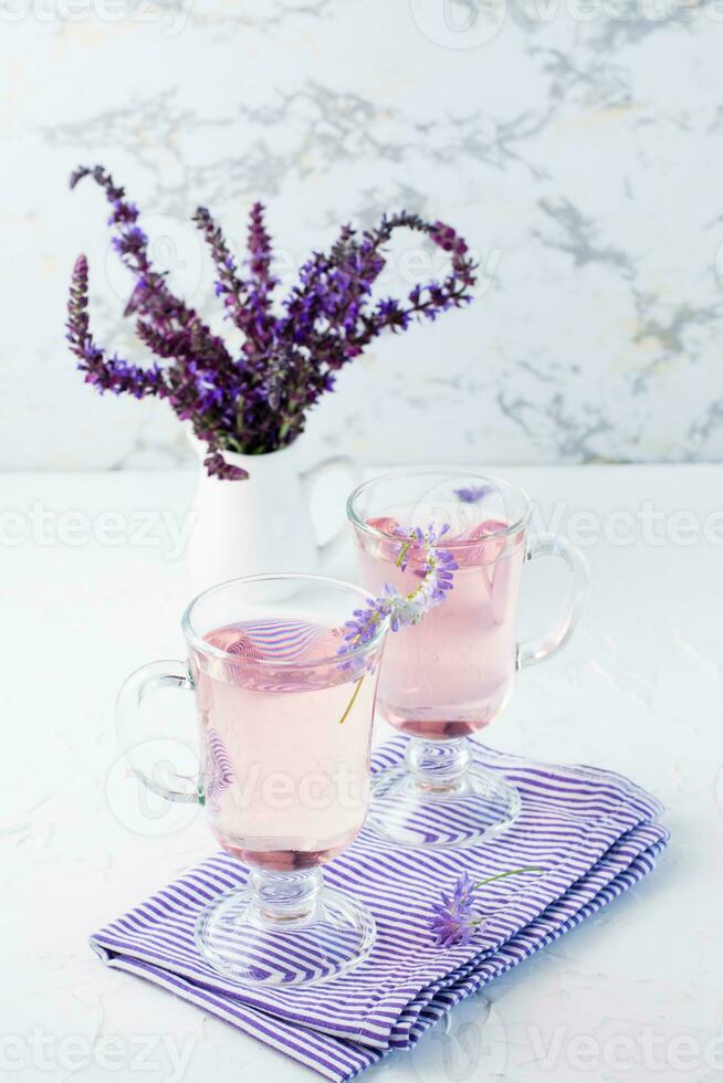 fresco acqua con lavanda nel bicchieri e un' mazzo di fiori nel un' brocca su il tavolo. lavanda aromatico cocktail. copia spazio. verticale Visualizza foto