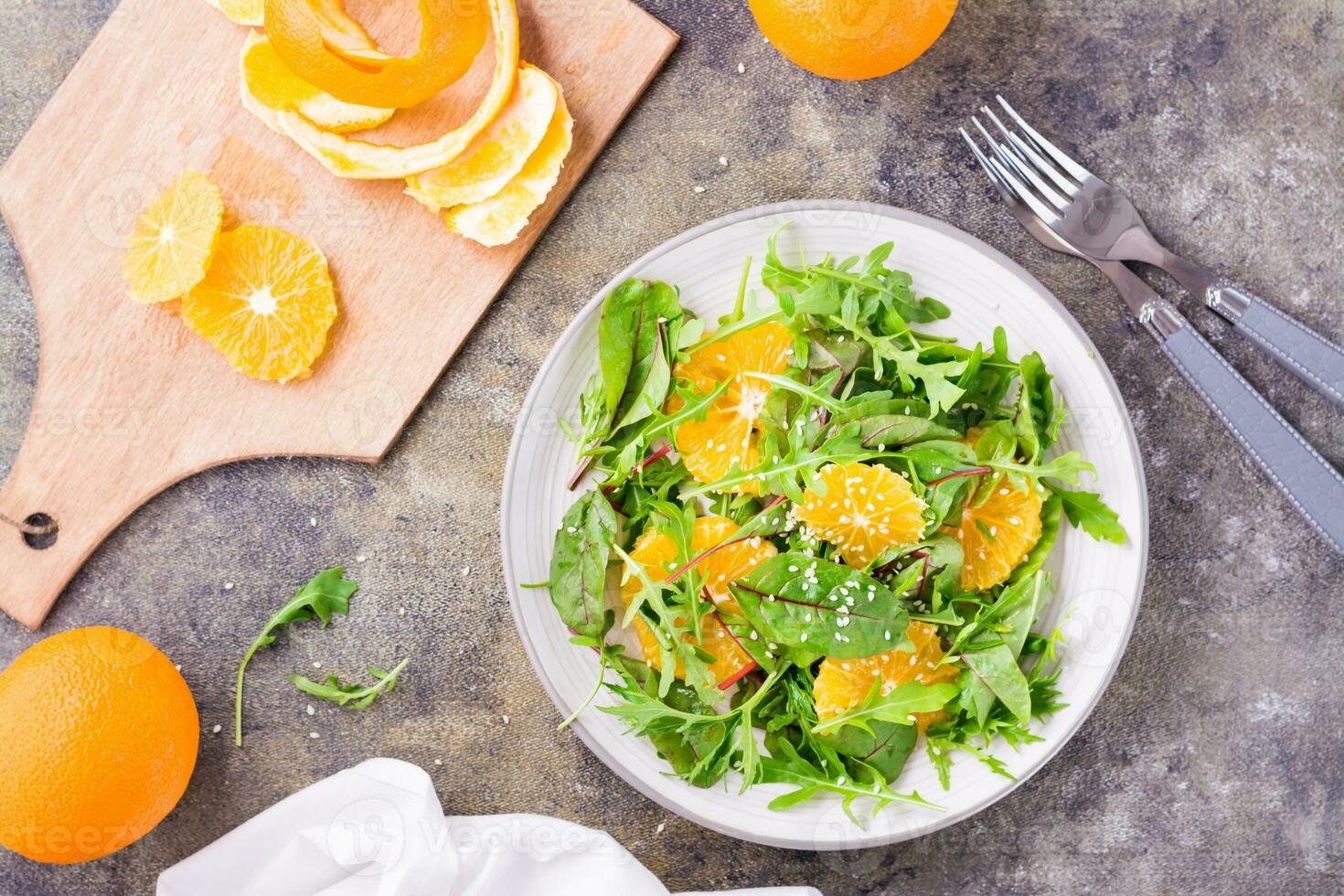 dieta vegetariano vitamina insalata di arancia fette e un' mescolare di rucola, bietola e mizun le foglie su un' piatto e un' taglio tavola con pelato arancia su il tavolo. superiore Visualizza foto