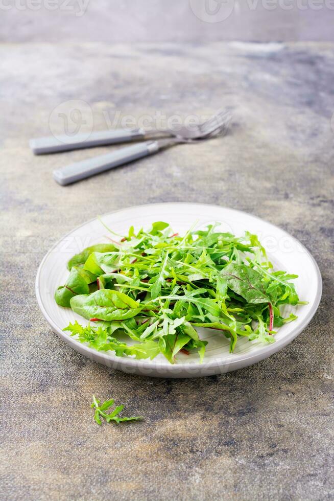 un' miscela di fresco rucola, bietola e mizun le foglie su un' piatto e forchette su il tavolo. vegetarianismo, salutare mangiare. verticale Visualizza foto