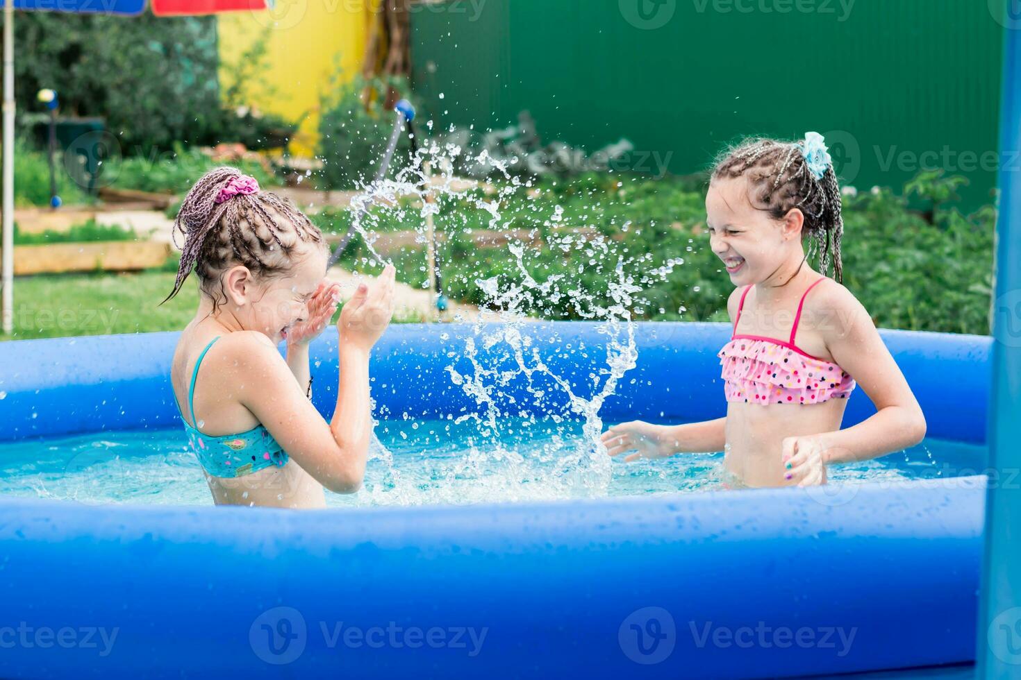 Due ragazze avere divertimento spruzzi nel un gonfiabile piscina su un' estate giorno nel il Giardino dietro la casa foto