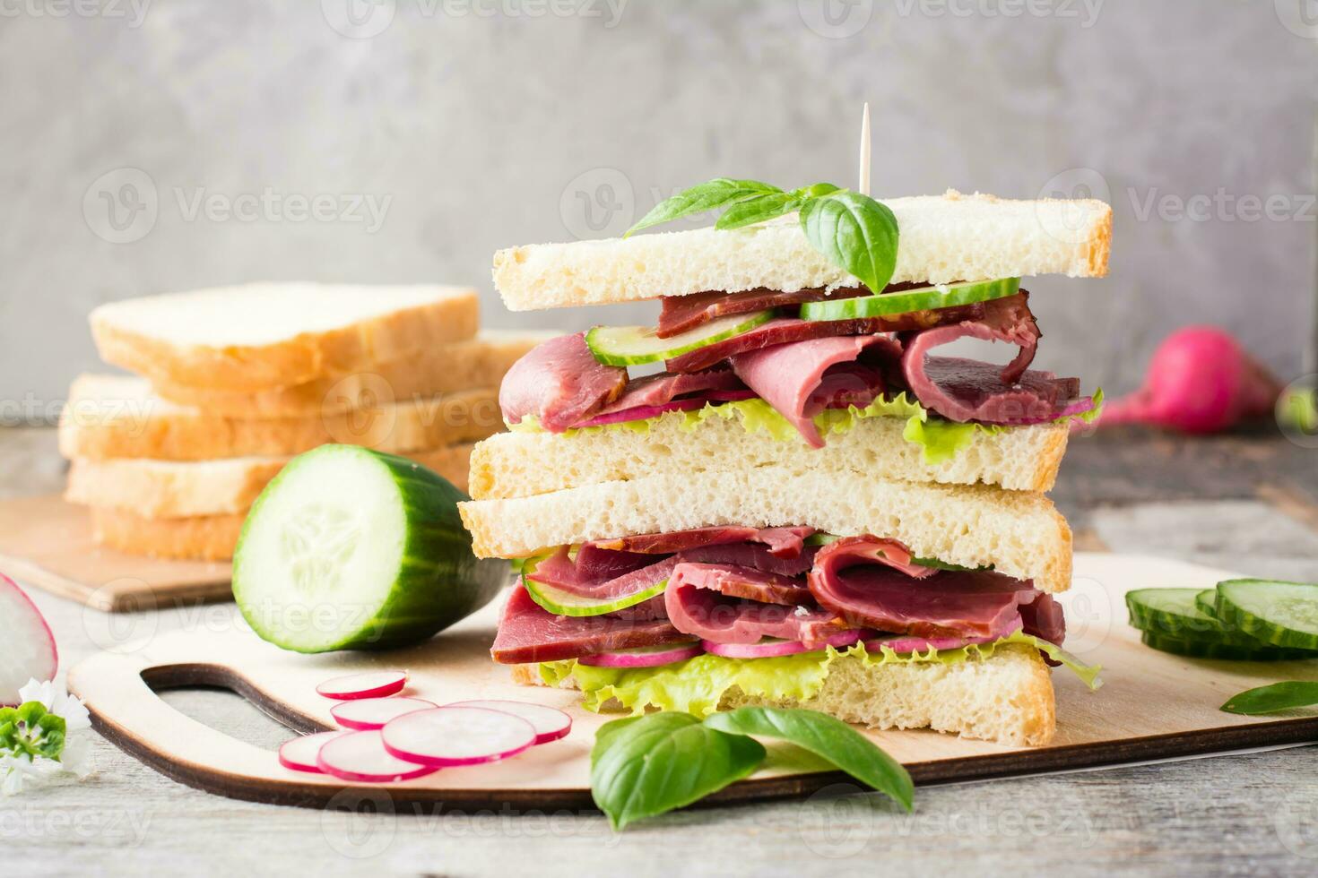 Doppio Sandwich con pasticcini, cetriolo, ravanello e basilico su un' taglio tavola. americano merenda. rustico stile foto