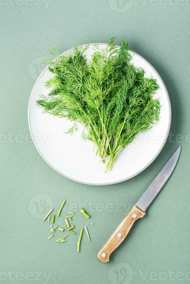 un' mazzo di fresco aneto su un' piatto, un' coltello e tagliare via steli su un' verde sfondo. vitamina verdura nel un' salutare dieta. superiore Visualizza foto