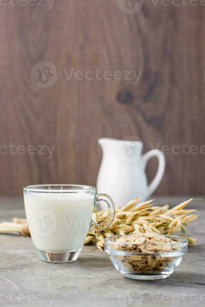 avena latte nel un' tazza, fiocchi d'avena e orecchie di Mais su il tavolo. alternativa per di mucca latte. verticale Visualizza foto