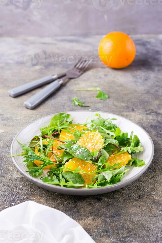 dieta vegetariano vitamina insalata di arancia pezzi e mescolare di rucola, bietola e mizun le foglie su un' piatto su il tavolo. verticale Visualizza foto