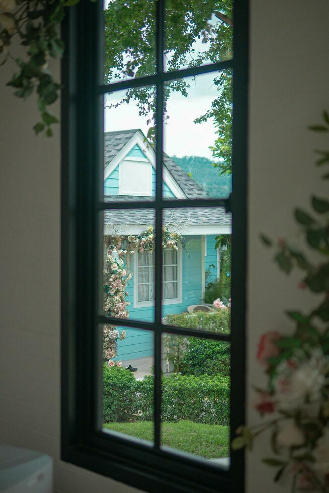 bellissimo Visualizza di il accogliente Casa circondato di verde alberi e un' blu cielo con nuvole nel il sfondo a partire dal il finestra. foto