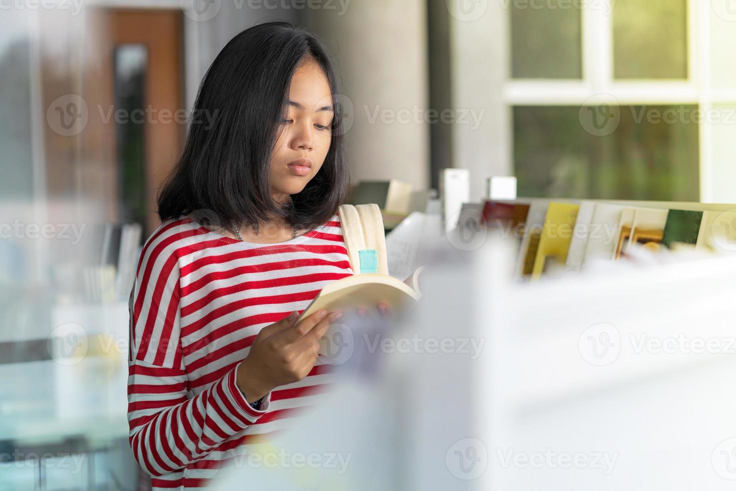 ragazza asiatica in piedi a leggere un libro in libreria foto