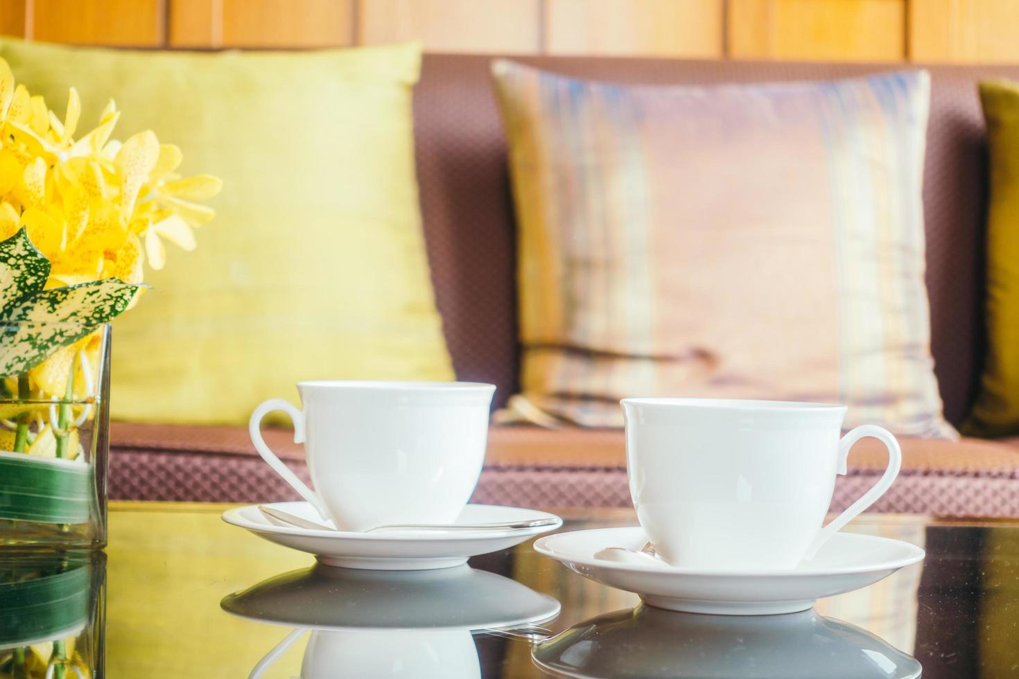 vaso di fiori e tazza di caffè bianco sul tavolo e cuscino sul divano foto