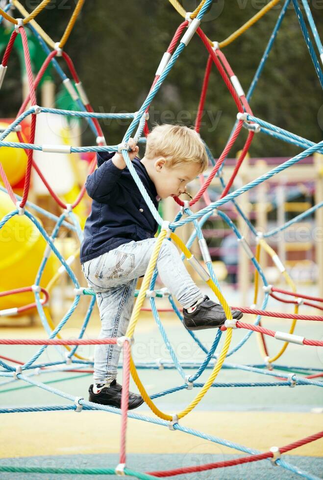 contento poco ragazzo arrampicata su terreno di gioco attrezzatura foto