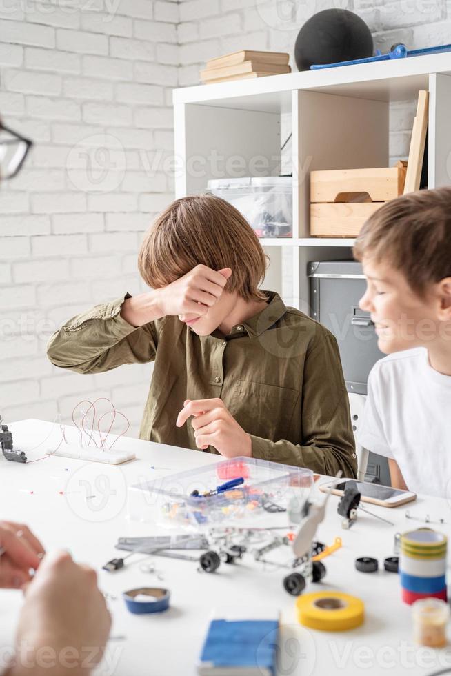 ragazzo stanco che lavora a un progetto di scienze asciugandosi la faccia foto