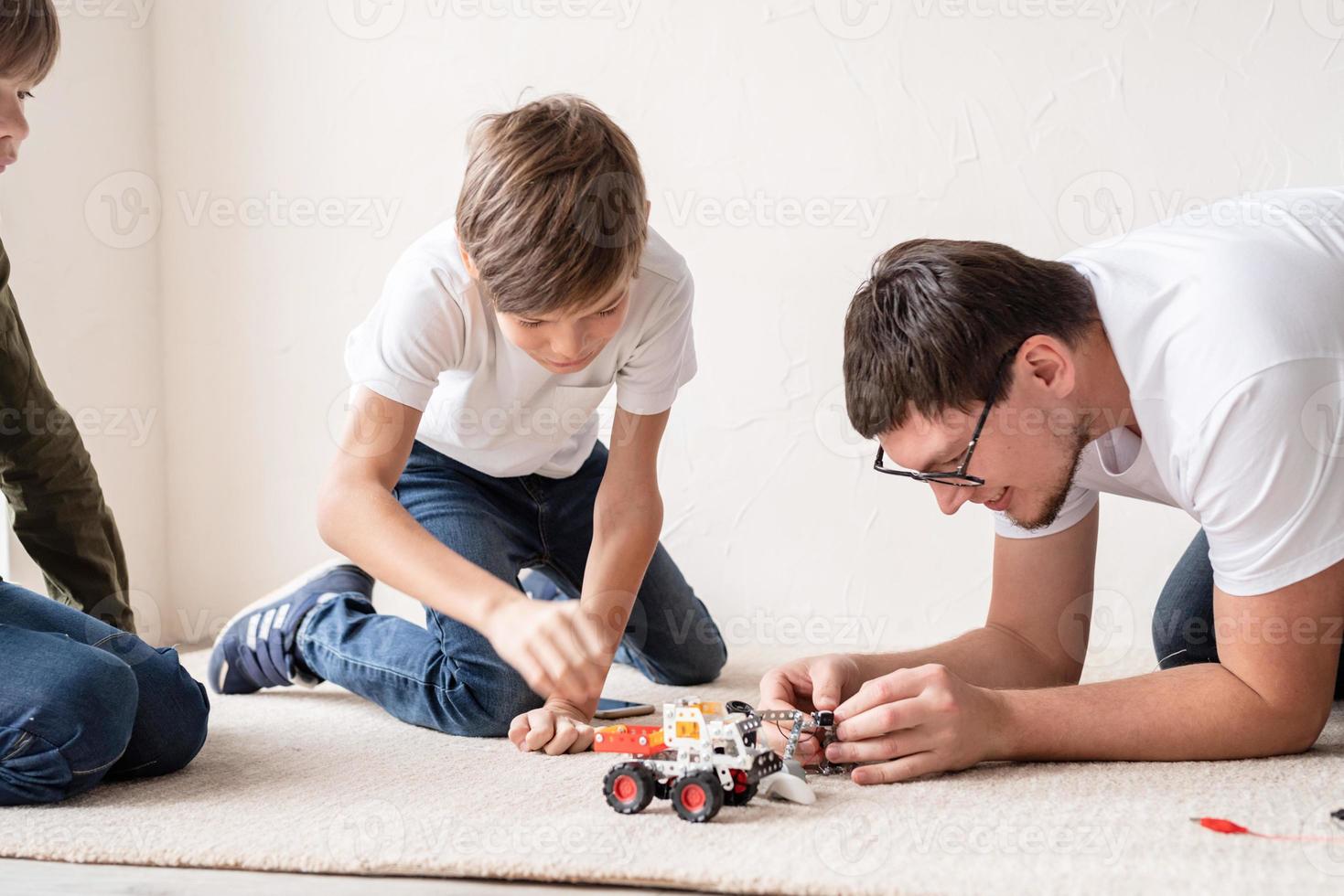 padre e ragazzi si divertono a costruire auto robot a casa seduti sul tappeto foto