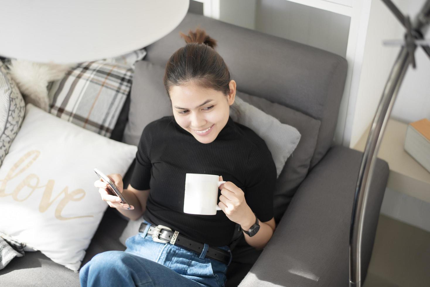 giovane bella donna che si rilassa sul divano di casa e usa lo smartphone foto