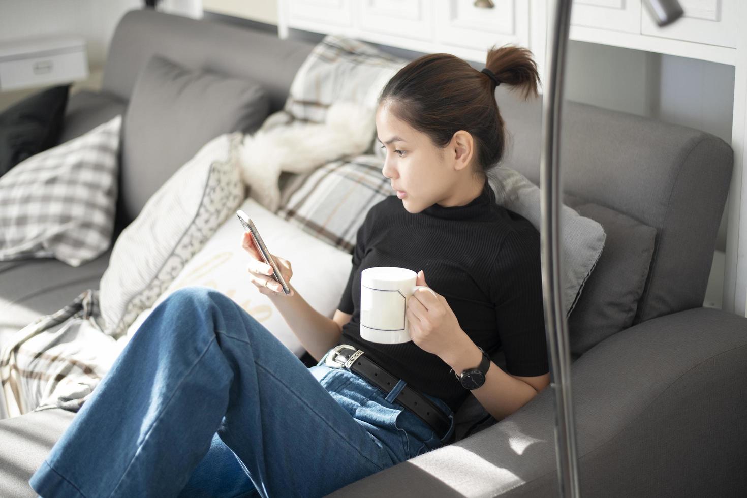 giovane bella donna che si rilassa sul divano di casa e usa lo smartphone foto