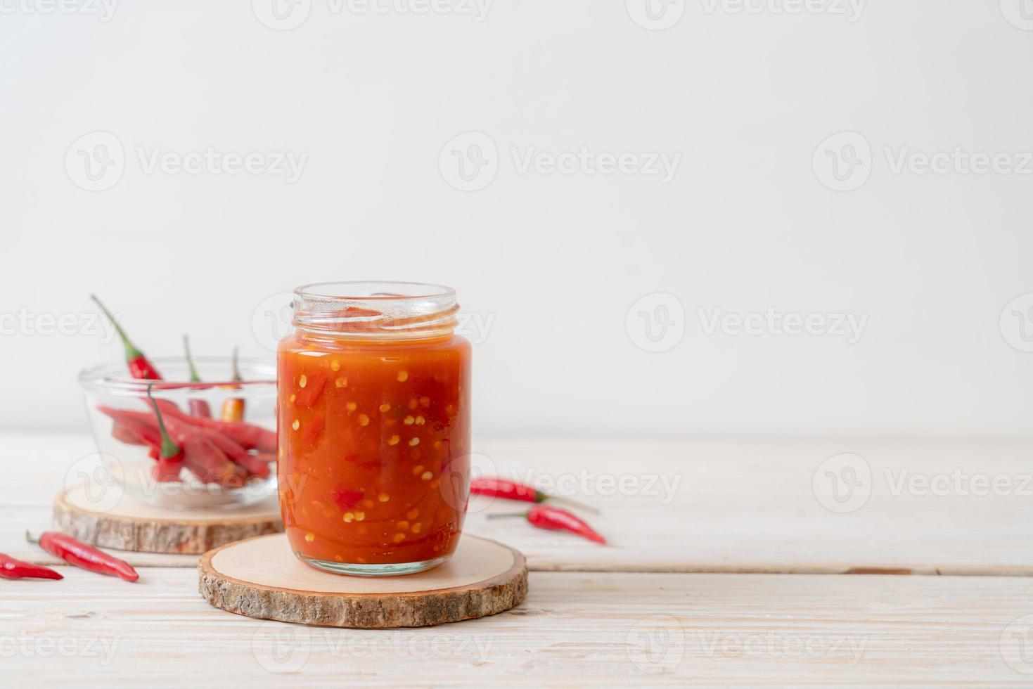 peperoncino o salsa di peperoncino in bottiglia e barattolo su fondo di legno foto