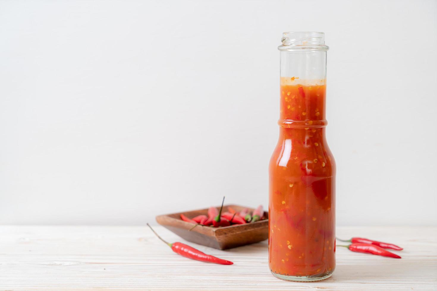 peperoncino o salsa di peperoncino in bottiglia e barattolo su fondo di legno foto