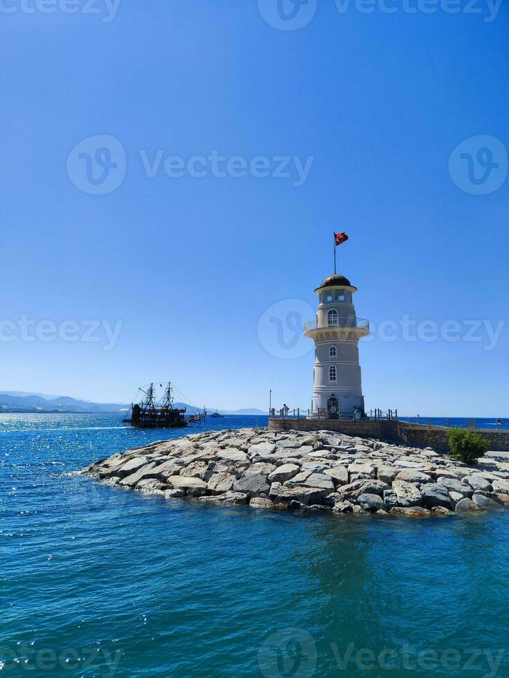 faro nel il mare con roccioso riva e chiaro blu acqua nel luminosa luce del sole foto