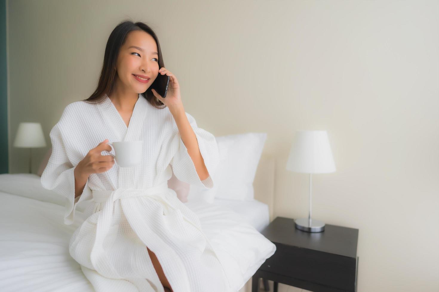 ritratto belle giovani donne asiatiche con tazza di caffè e telefono cellulare sul letto foto