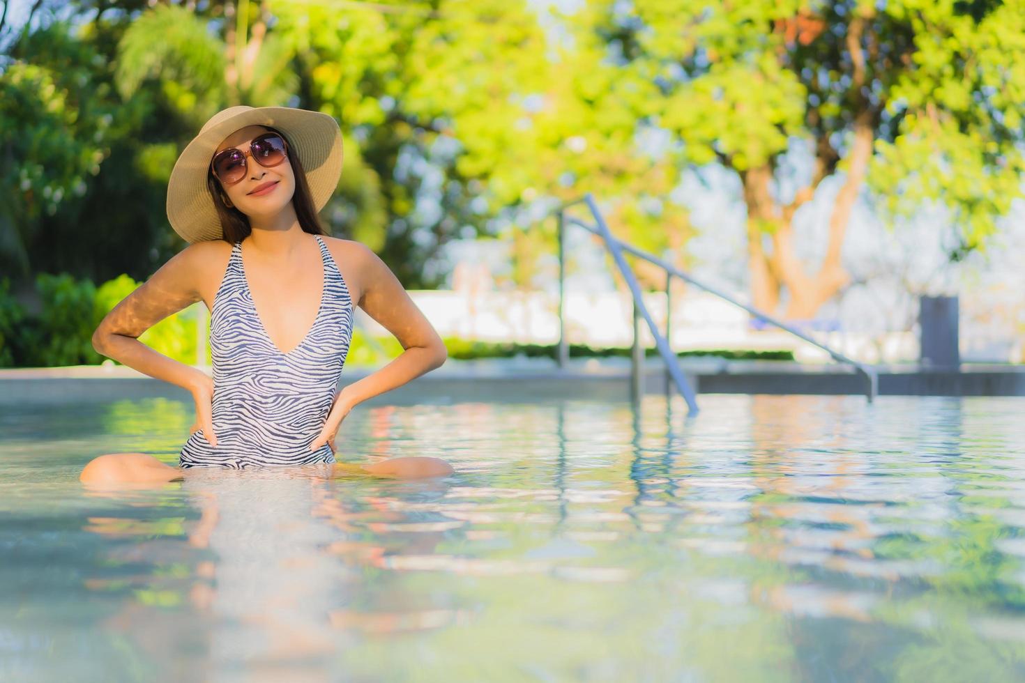 il sorriso felice delle belle giovani donne asiatiche si rilassa intorno alla piscina all'aperto nel resort dell'hotel per i viaggi in vacanza foto