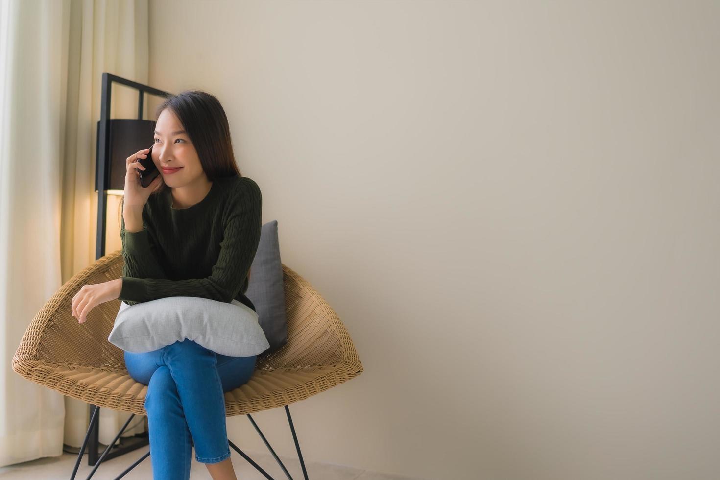 ritratto belle giovani donne asiatiche che usano il telefono cellulare e si siedono sulla poltrona del divano foto