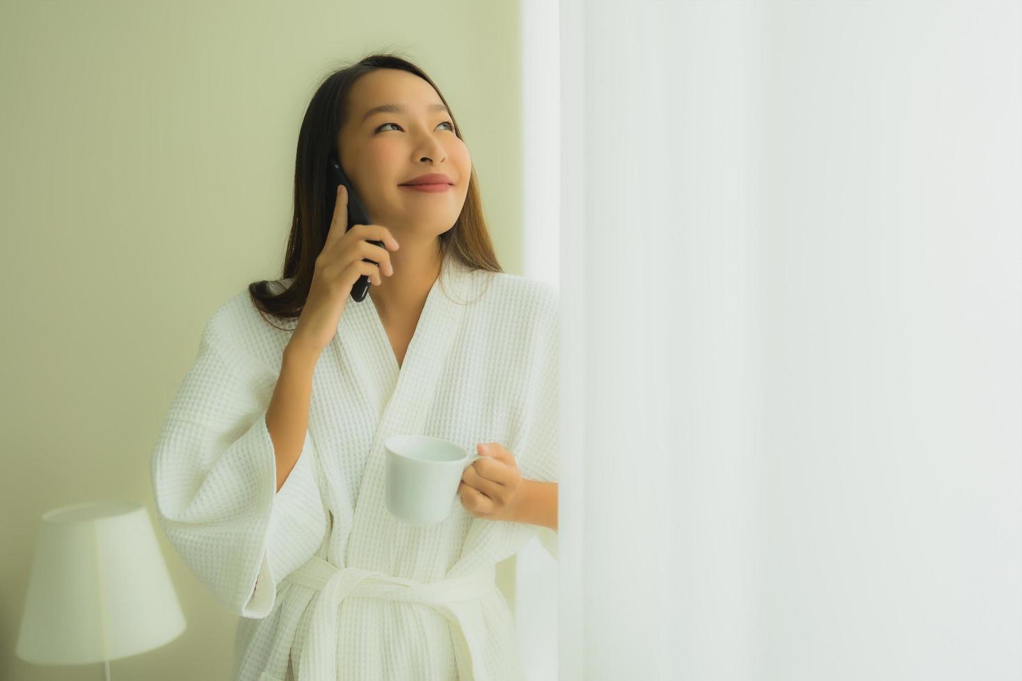 ritratto belle giovani donne asiatiche con tazza di caffè e telefono cellulare sul letto foto