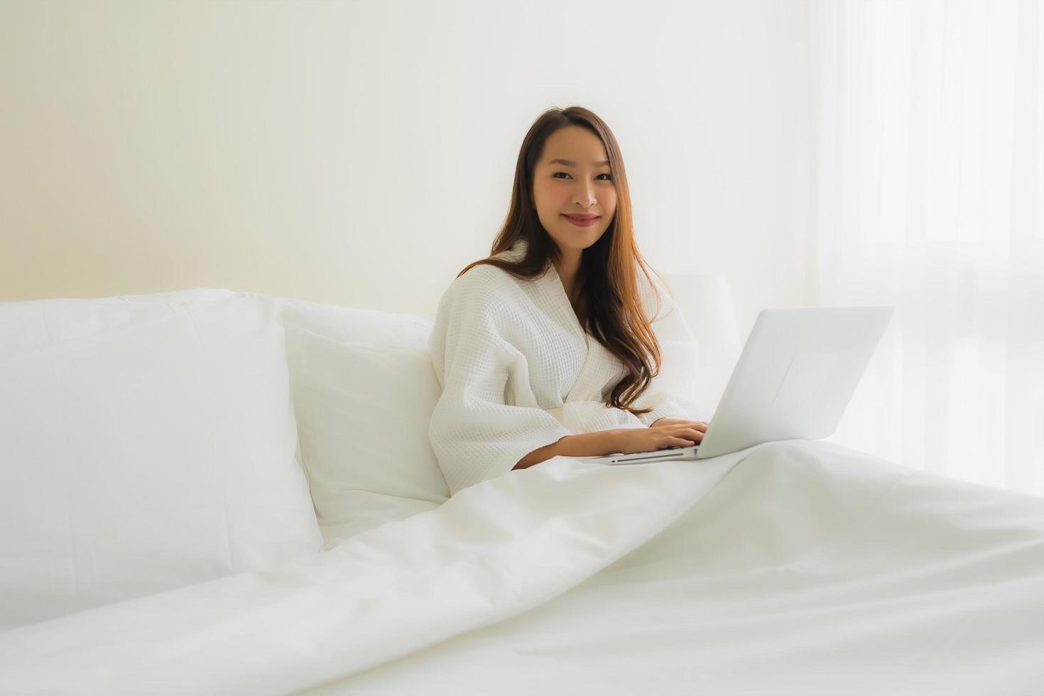 ritratto belle giovani donne asiatiche con tazza di caffè e computer portatile sul letto foto