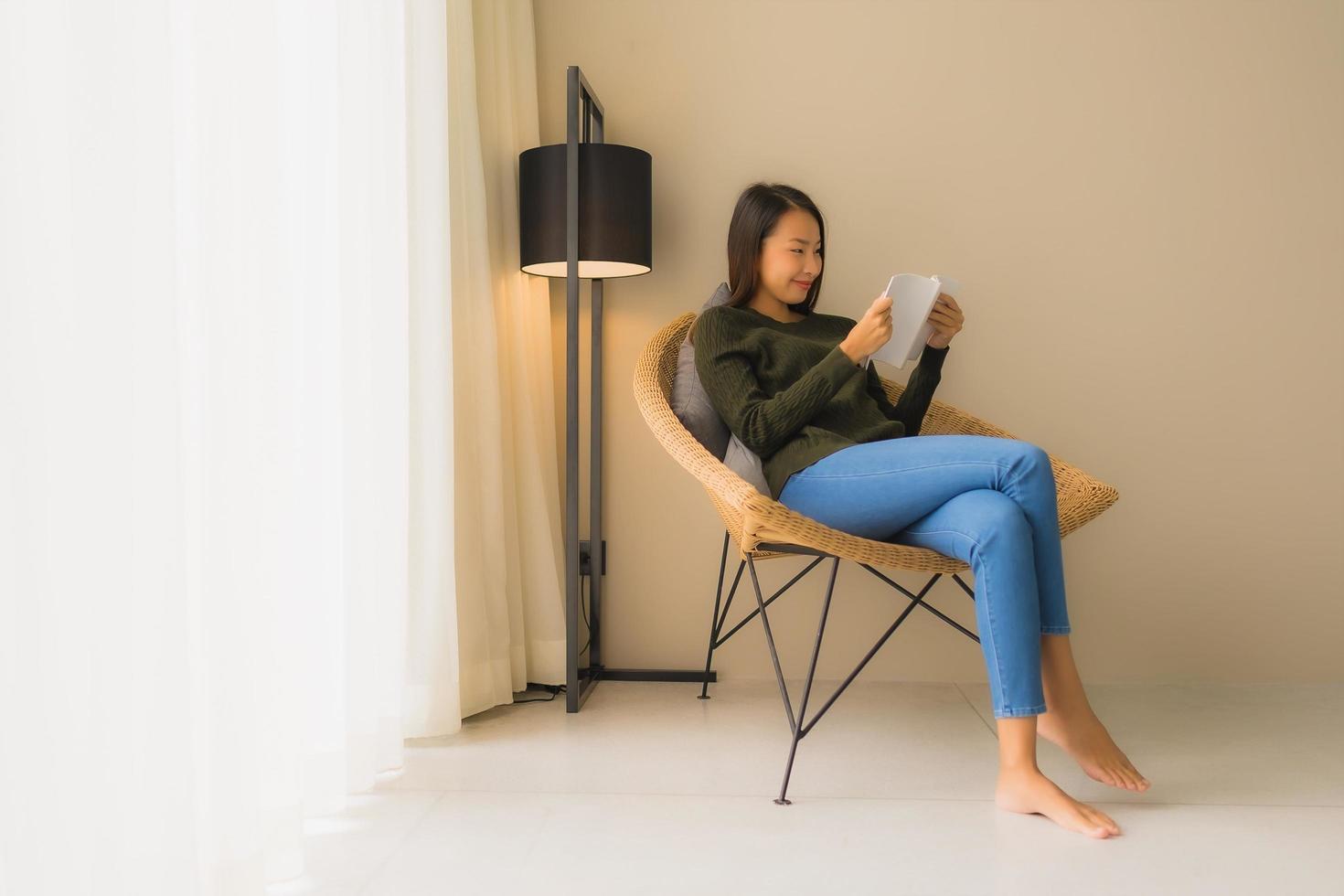 ritratto belle giovani donne asiatiche che leggono libri e si siedono sulla poltrona del divano foto