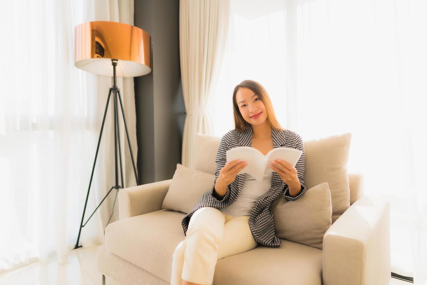 ritratto belle giovani donne asiatiche che leggono libri e si siedono sulla poltrona del divano foto