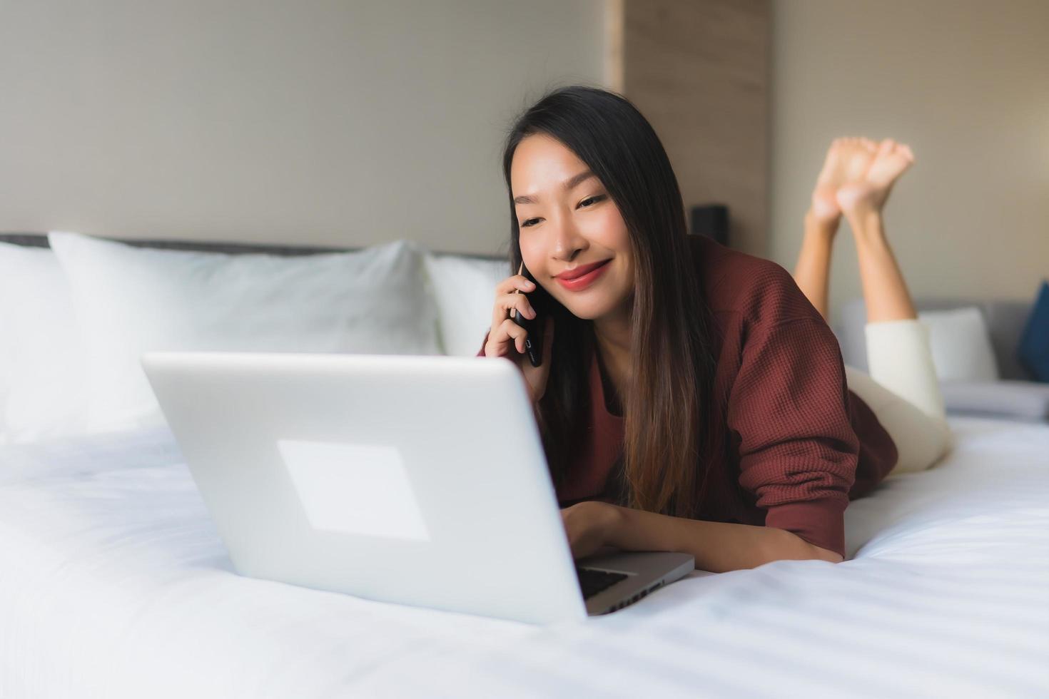 ritratto belle giovani donne asiatiche che utilizzano computer e telefono cellulare sul letto foto