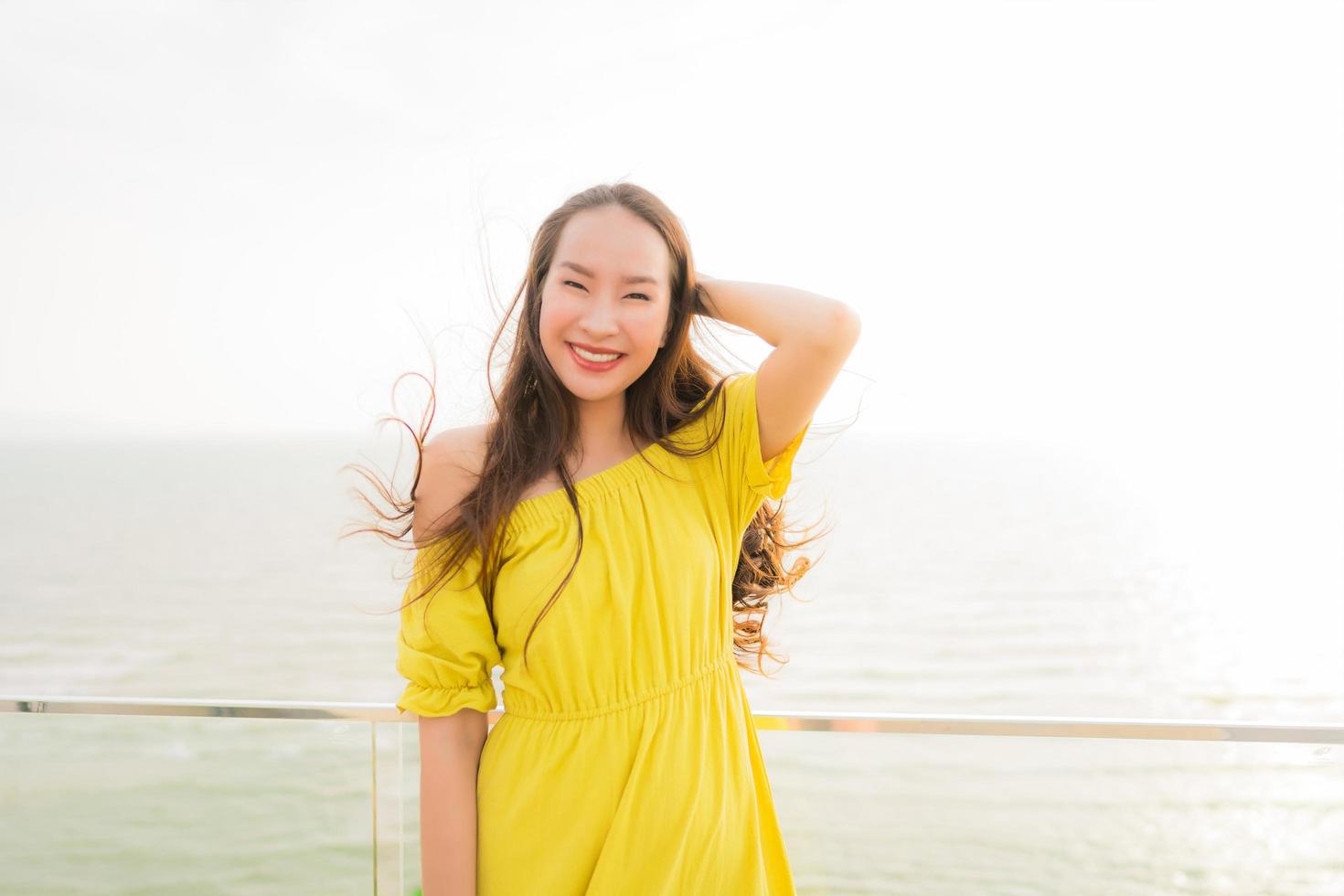 ritratto bella giovane donna asiatica sorridere felice e rilassarsi sul balcone all'aperto con spiaggia del mare e vista sull'oceano foto