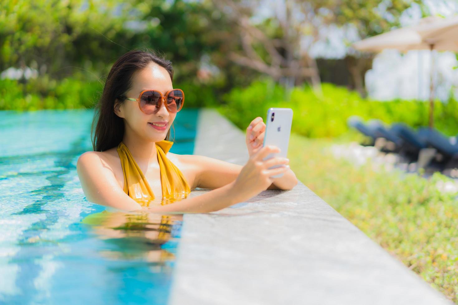 ritratto bella giovane donna asiatica che utilizza il telefono cellulare o il cellulare in piscina foto
