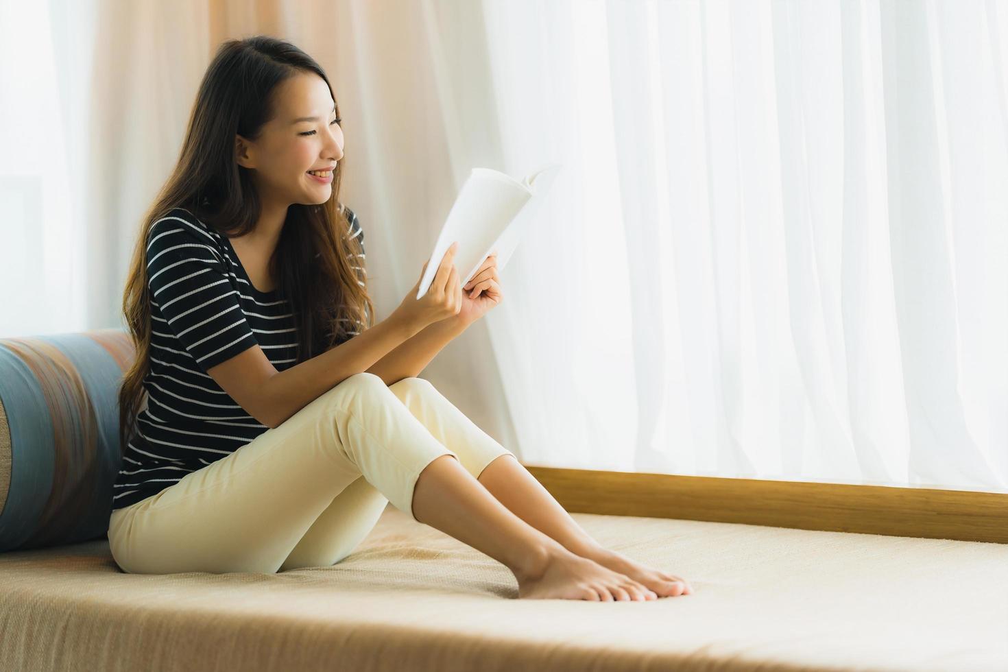 Ritratto di bella giovane donna asiatica che legge un libro sul divano nell'area soggiorno living foto