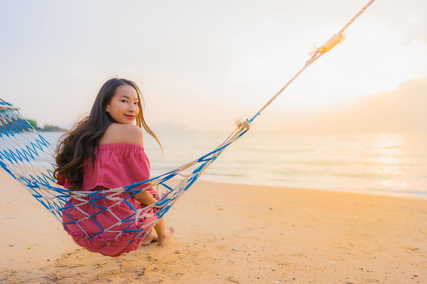 ritratto bella giovane donna asiatica seduta sull'amaca con sorriso felice spiaggia vicina mare e oceano foto