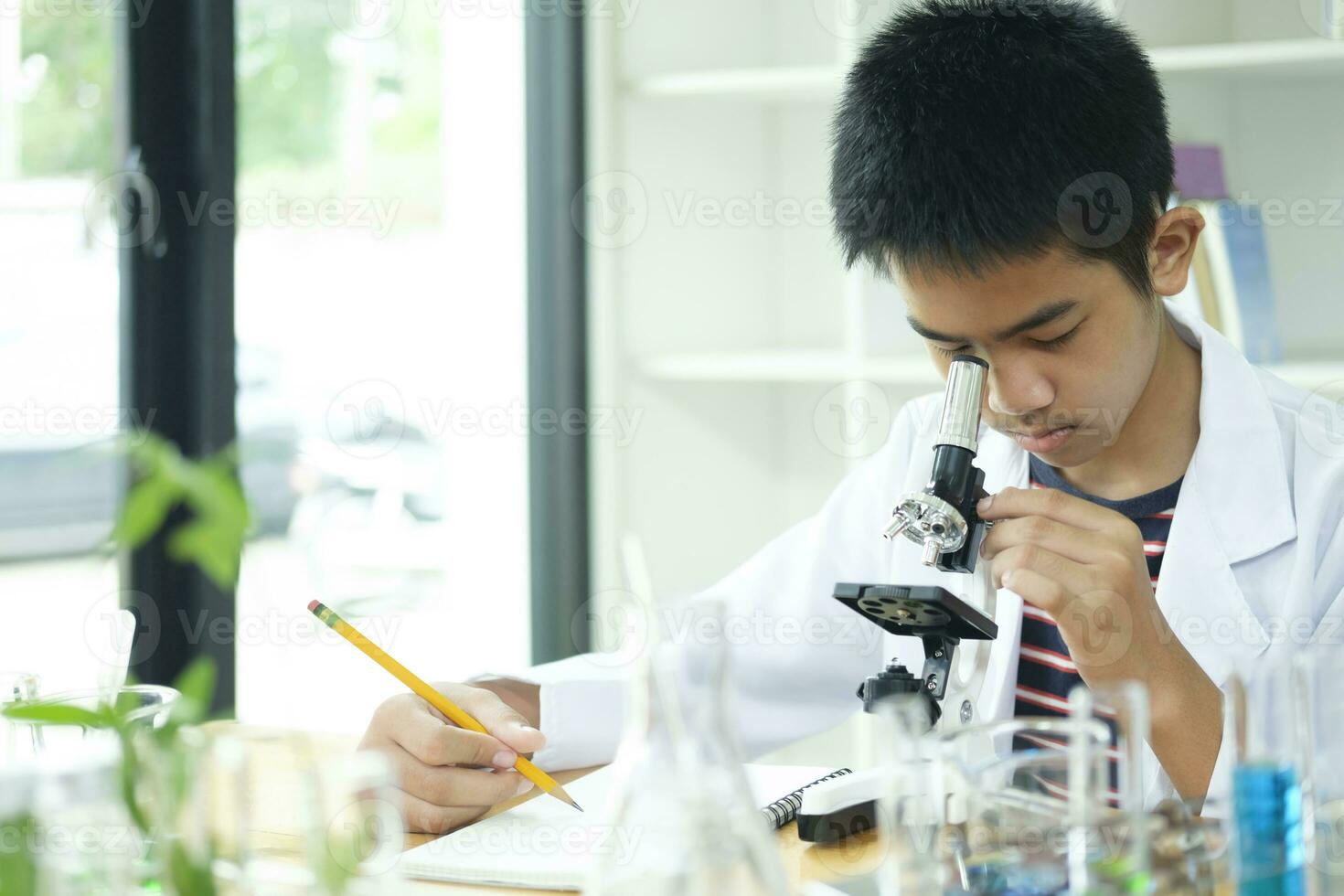giovane scienziato elementare scolaro esplora con microscopio foto